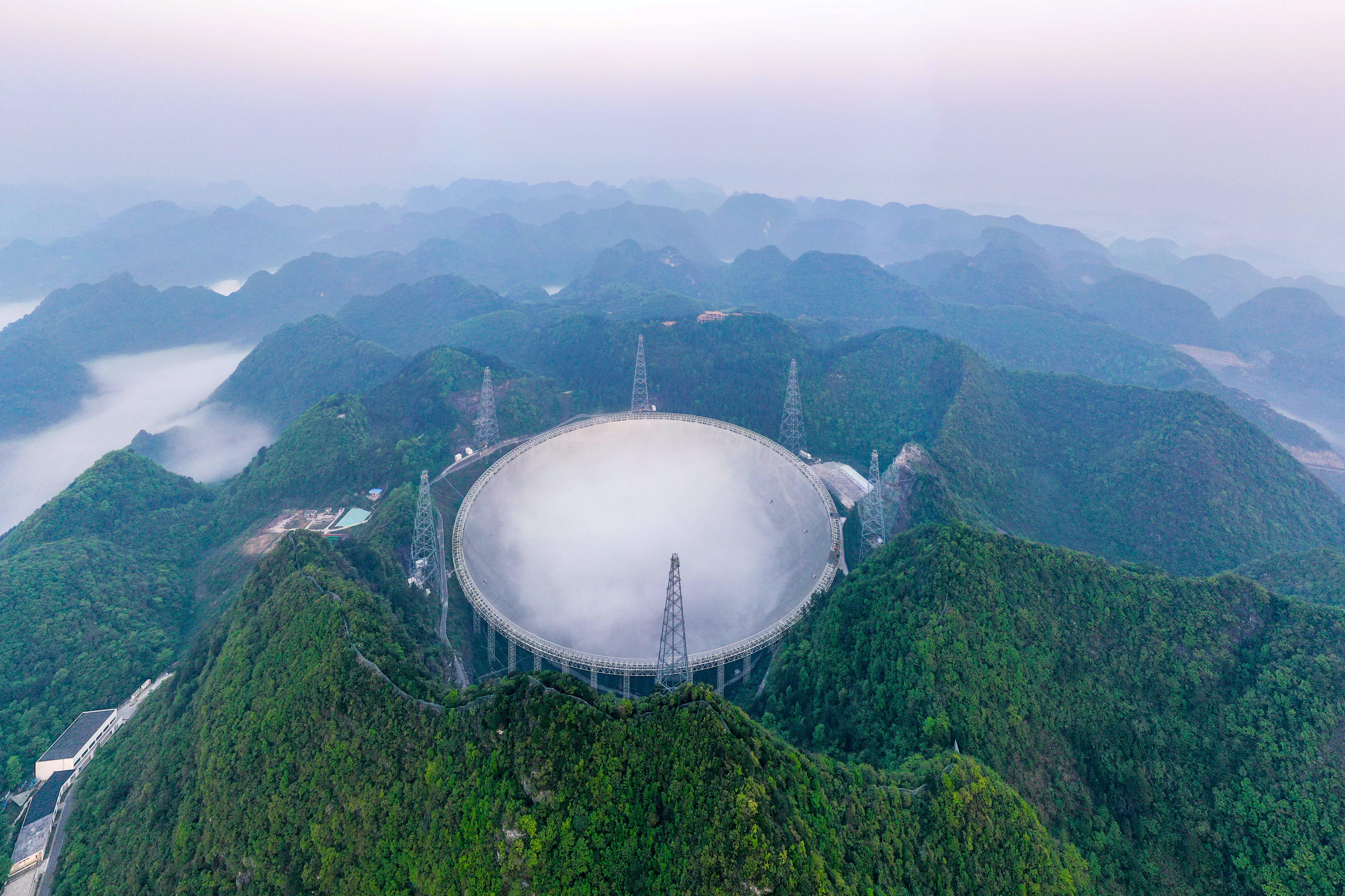 A giant spherical dish-shaped telescope on the top of a mountain.