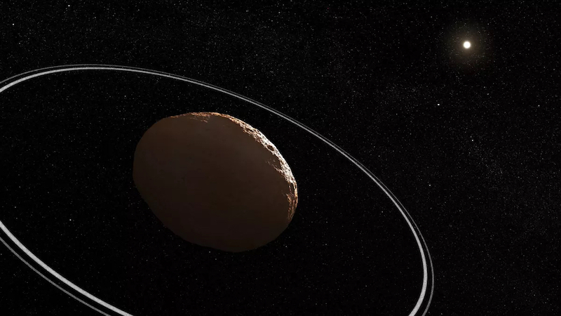 Egg-shaped rocky body with 2 thin rings around it and distant sun and stars in background.
